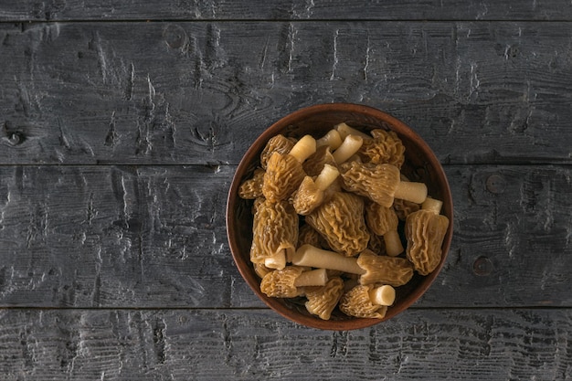 Глиняная миска со свежесобранными сморчками на темном деревянном фоне Первые весенние грибы