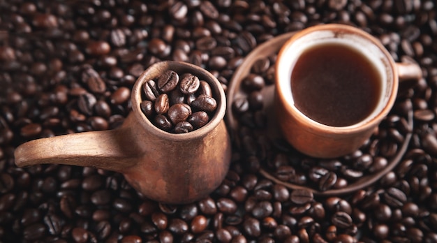 Clay coffee cup and pot on coffee beans.