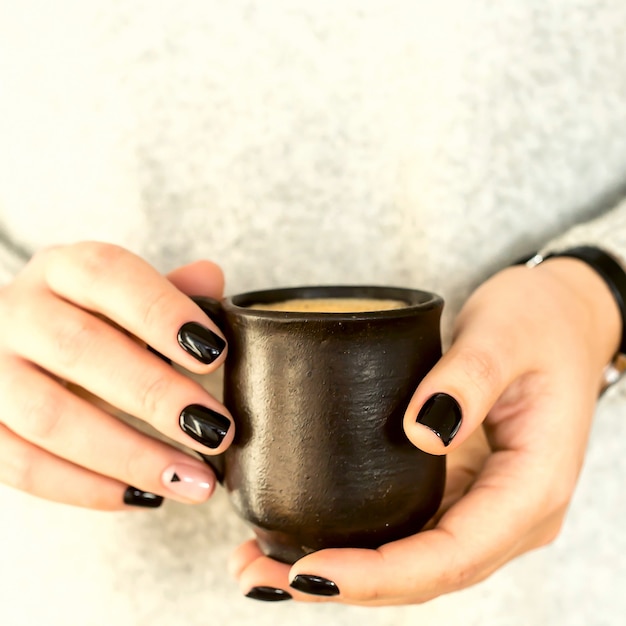 Tazza di argilla con caffè nelle mani di una ragazza con una manicure minimalista nera