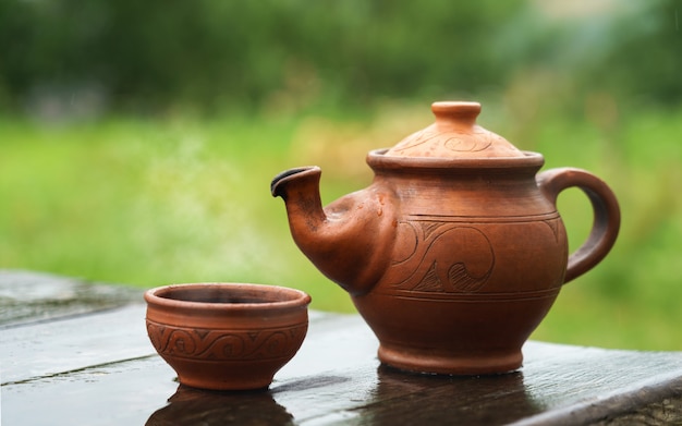 Clay hand made teapot and cup on wooden table outdoor with rainy weather