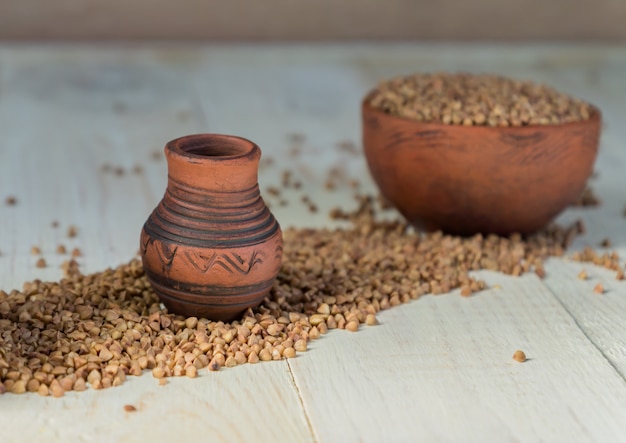 Clay jars for milk and buckwheat scattered on wooden table. 