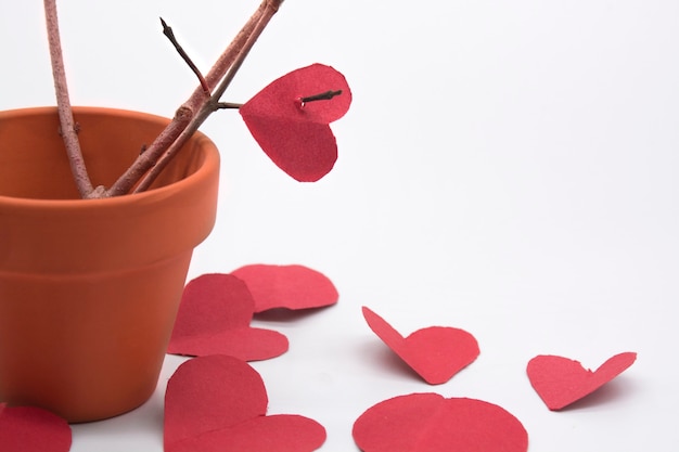 バレンタインデーのための茶色の木の枝と鍋の周りの赤いハートの粘土ミニポット