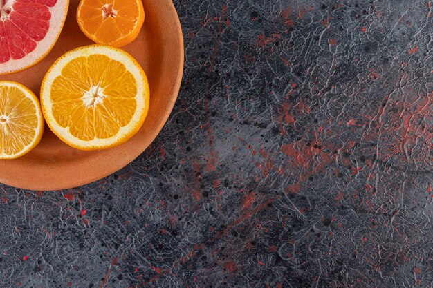 Clay plate with sliced orange, lemon and grapefruit on marble surface