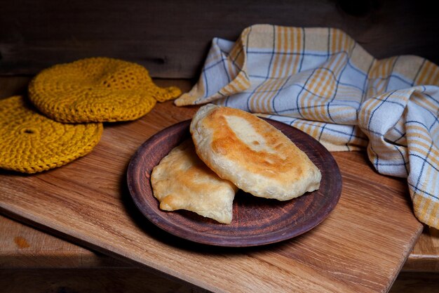 Clay plate with two of individual fried pies with meat on wooden table tatar traditional pies