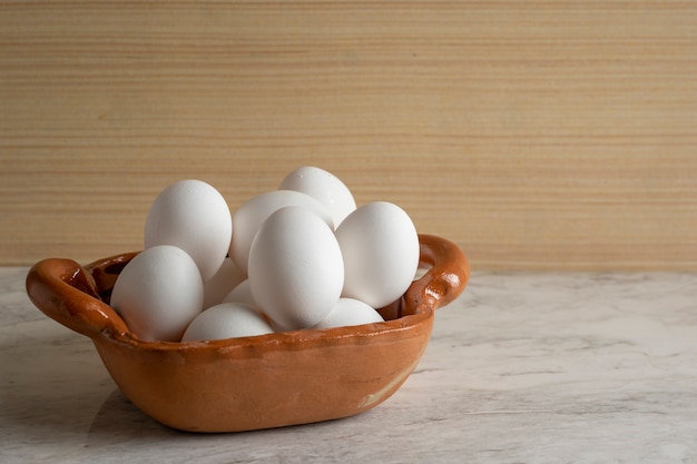 Clay pot filled with white eggs on a marble bar and wooden bottom