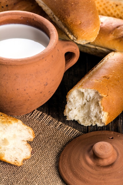 Clay pot met melk en stokbrood op houten tafel