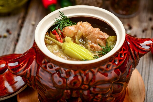 Clay pots with baked potatoes and chicken meat on wooden plank.