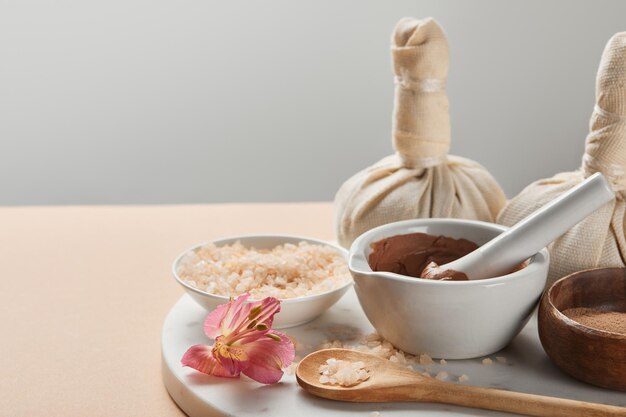 Photo clay and sea salt in bowls on marble surface with flower and decora isolated on grey