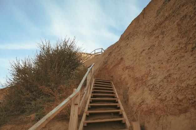 Clay slope with wooden steps against blue sky