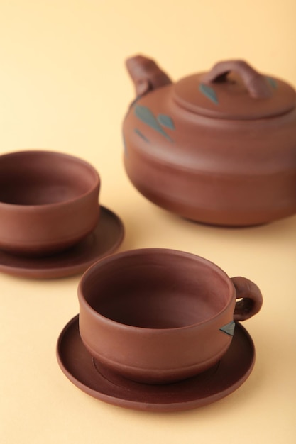 Clay teapot with cups on beige background