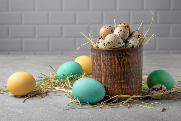 A clay vessel with quail eggs in hay surrounded by painted chicken eggs