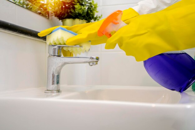 Clean the bathroom faucet concept wear yellow rubber gloves spray the detergent and scrub with a sponge White sanitary ware