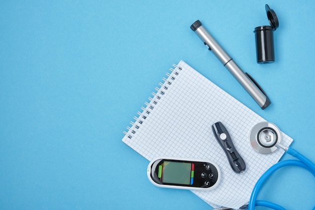 Clean block with spring, stethoscope, glucose meter, lancet and syringe pen with insulin on a blue background, daibet day concept, diabetes diagnosis