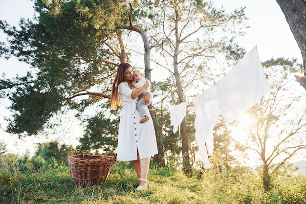 Clean clothes hanging on the rope to dry Young mother with her little son is outdoors in the forest Beautiful sunshine