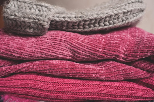 Clean cotton knitted sweaters and hat stacked in wardrobe closeup. Winter season.