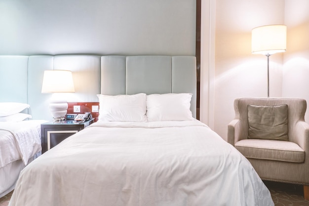 깨끗하고 아늑한 현대적인 호텔 침실은 고급 여행의 쿠션 디자인 컨셉을 갖춘 스탠딩 램프 린넨 소파가 있는 따뜻한 톤의 객실입니다.