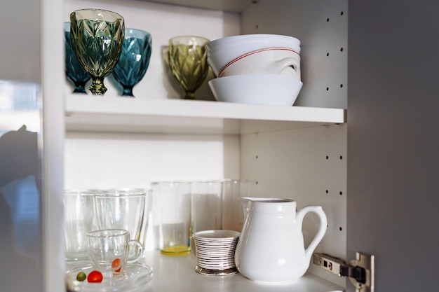 Clean dishes and tableware on white shelf