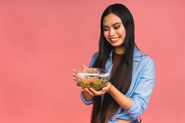 Clean eating diet concept Asian woman holding vegeterian salad or bowl in take away container Close up copy space isolated over pink background