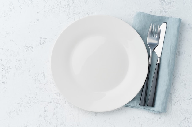 写真 空の白い皿、フォーク、白い石のテーブルの上のナイフ、コピースペース、上面図。