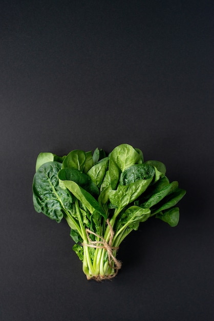 Clean food concept. Bunch of leaves of fresh organic spinach greens on a black background. Healthy detox spring-summer diet. Vegan Raw Food. Copy space.