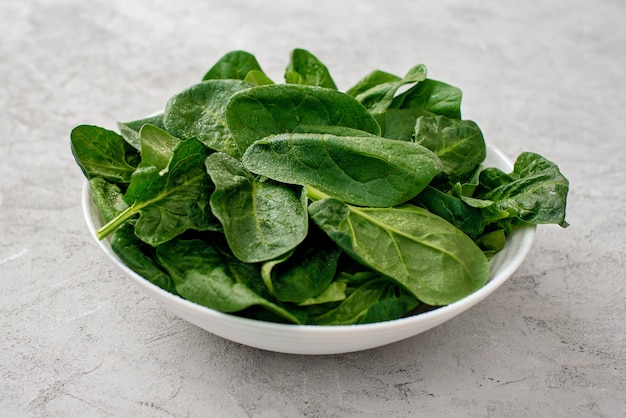 Photo clean food concept. leaves of fresh organic spinach greens in a plate on a light background. healthy detox spring-summer diet. vegan raw food.