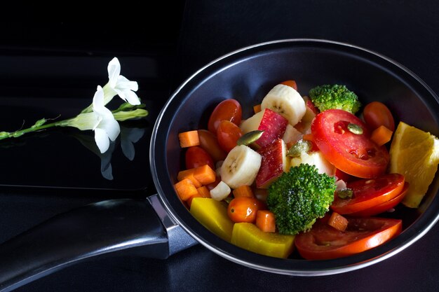 Cibo pulito, mescolare frutta ed erba in padella su sfondo scuro