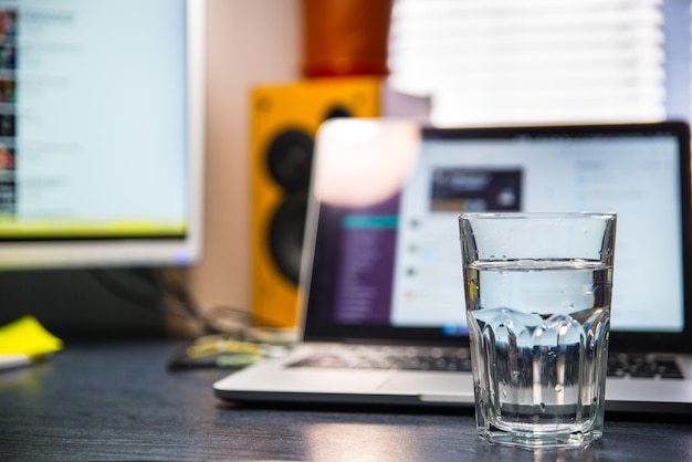 Фото Чистый стакан воды на столе. ноутбук на фоне