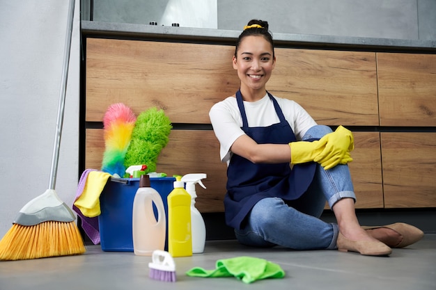 Clean Home. Full length shot of happy young woman smiling at camera while resting after cleaning floor with detergents. Housework and housekeeping, cleaning service concept