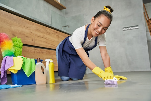 Clean it up. Full length shot of joyful young woman smiling while cleaning floor with detergents at home. Housework and housekeeping, cleaning service concept. Low angle view