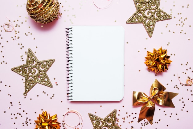 Foto notebook pulito per obiettivi o lista del negozio di natale e risoluzioni su sfondo rosa con stelle decorative dorate e coriandoli