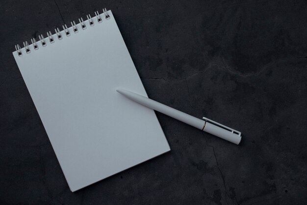 Photo clean notepad and pen on dark background with texture. concept for education or business with space for text. notebook with white paper for writing notes, top view.