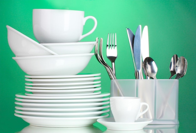 Clean plates cups and cutlery on green background