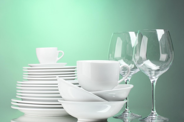 Clean plates cups and glasses on green background