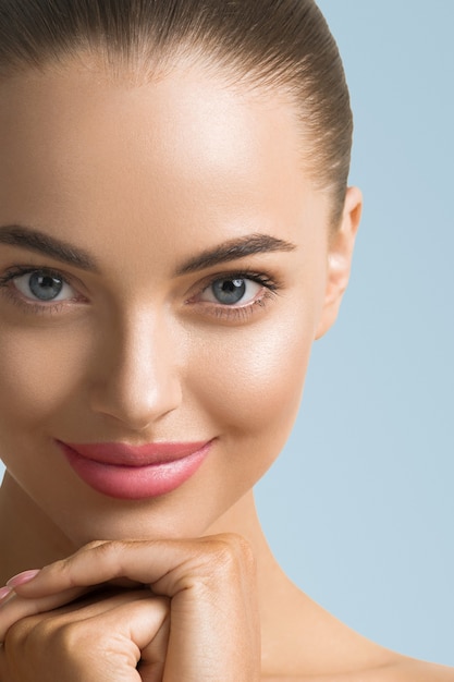 Clean skin woman face close up beauty tanned face beautiful smile. Blue background. Touching face.