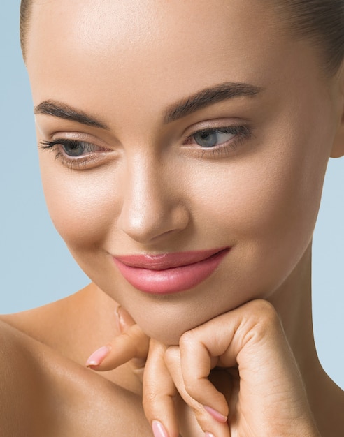 Clean skin woman face close up beauty tanned face beautiful smile. Blue background. Touching face.