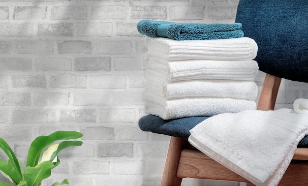 Clean terry towels on wooden chair with brick wall background, copy space.