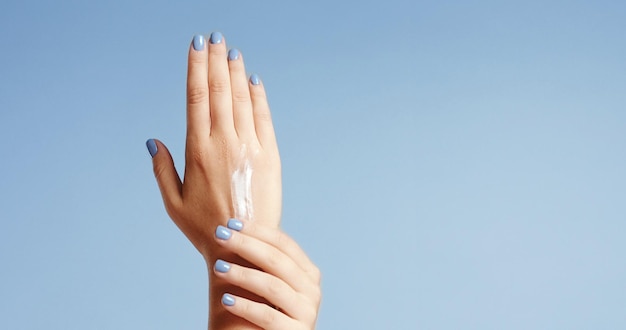 Чистые хорошо ухоженные руки молодой женщины, применяющей крем для рук по уходу за кожей на голубом фоне