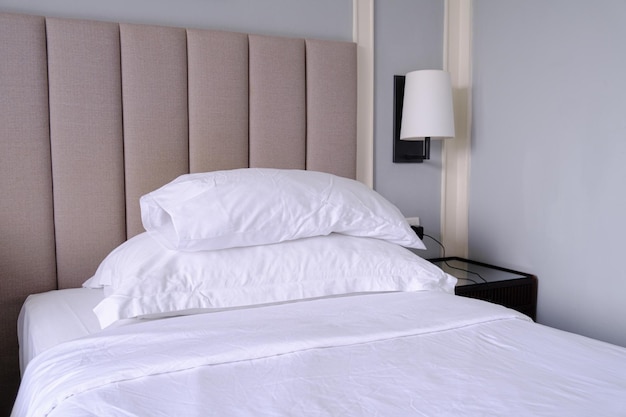 Clean white bed in the bedroom Bed with white linens bedside table and wall sconce