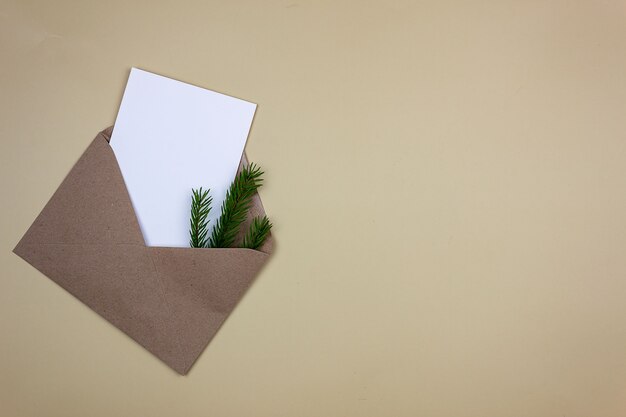 トウヒの小枝が付いている茶色の封筒のきれいな白いシート。招待状とグリーティングカードのモックアップ。