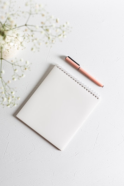 A clean white spiral notebook lies on a white structural background There is a pink pen next to it