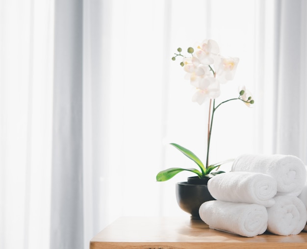 Clean white towels and beautiful orchid flowers on wood table with blurred white bathroom background