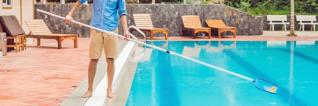 Cleaner of the swimming pool man in a blue shirt with cleaning equipment for swimming pools sunny