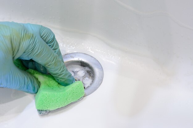 Cleaning the bathroom. Woman is cleaning sink and faucet with a sponge in rubber gloves and spray detergent. Close-up. Copy space.