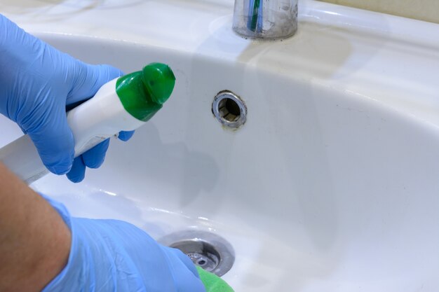 Cleaning the bathroom. Woman is cleaning sink and faucet with a sponge in rubber gloves and spray detergent. Close-up. Copy space.