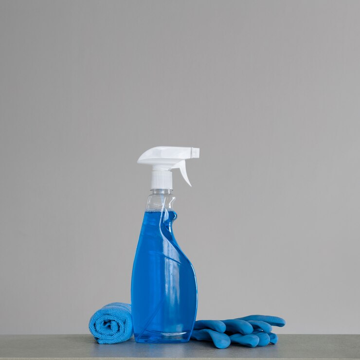 プラスチック製のディスペンサー、マリーゴールド、灰色のほこり用の布で青いスプレーボトルを掃除する