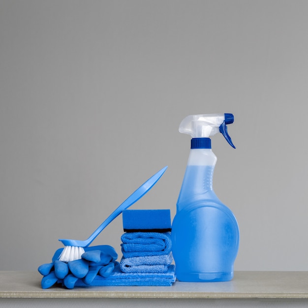 Cleaning blue spray bottle with plastic dispenser, sponge, scrubbing brush for dish, cloth for dust and rubber gloves on grey