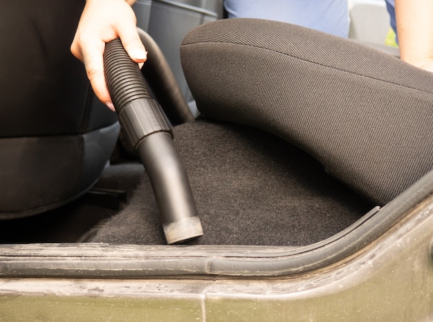 Cleaning the car, the girl collects the crumbs with a vacuum cleaner in the car