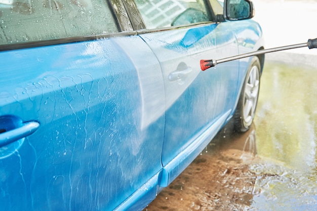 Cleaning car with high pressure water at car wash station