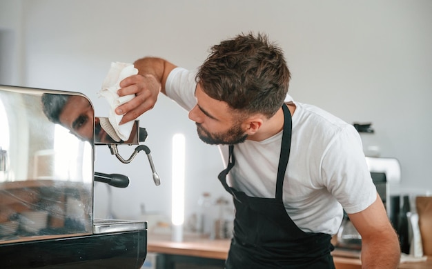 Foto pulizia della macchina da caffè il lavoratore del caffè in camicia bianca e grembiule nero è al chiuso