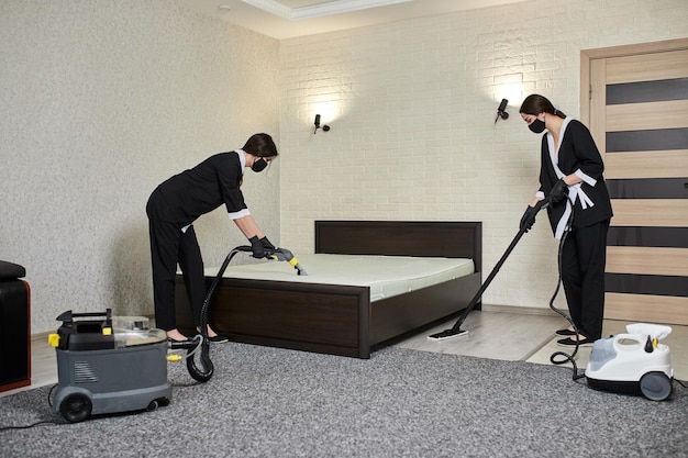 Cleaning company employees remove dirt from furniture in the\
apartment using professional equipment housewife women cleaning the\
mattress and floor with washing and steam vacuum cleaners